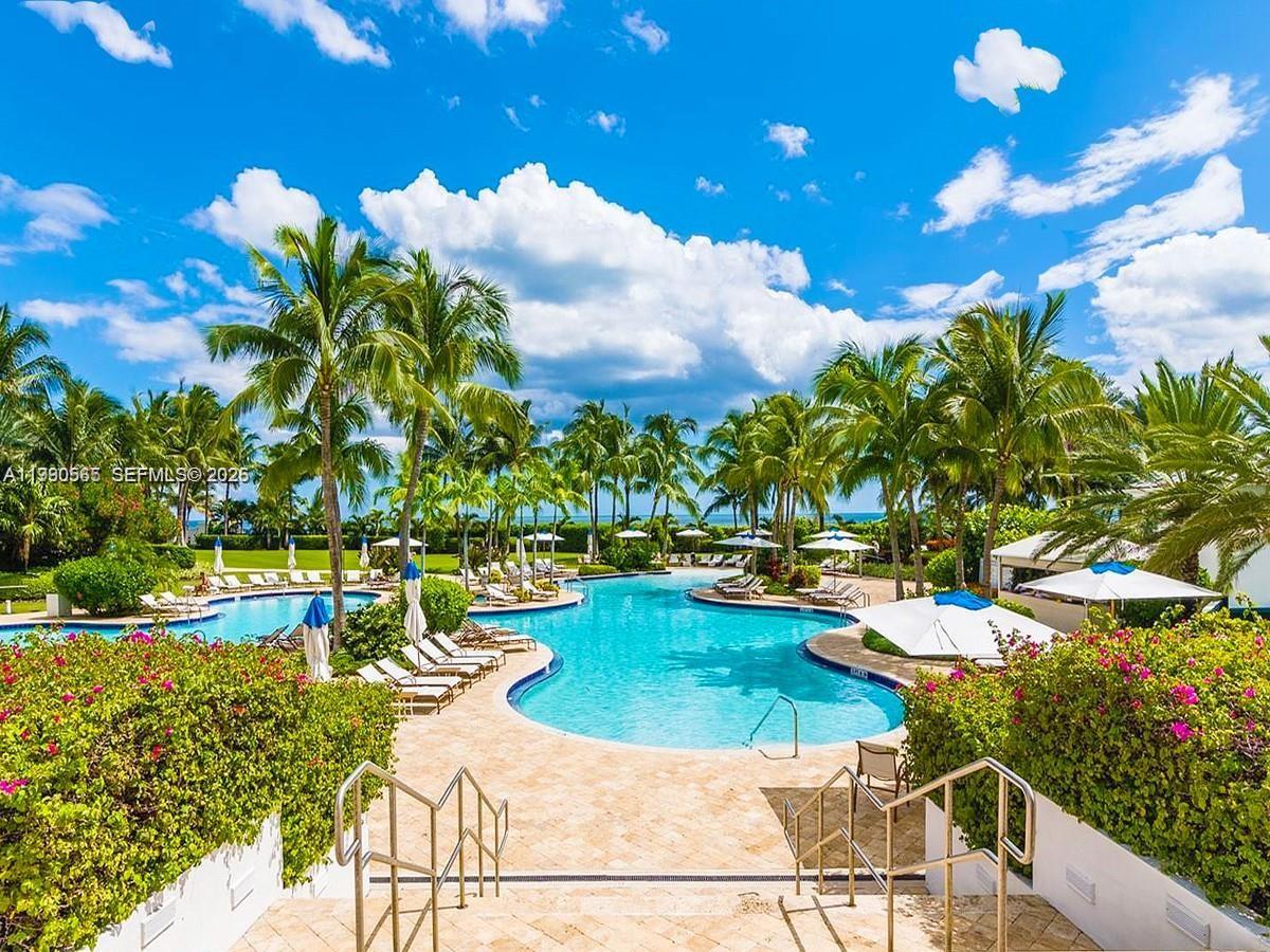 A swimming pool surrounded by palm trees, lounge chairs, and umbrellas under a blue sky — 50 S Pointe Dr # 504, Miami Beach FL 33139, MIAMI BEACH, FL