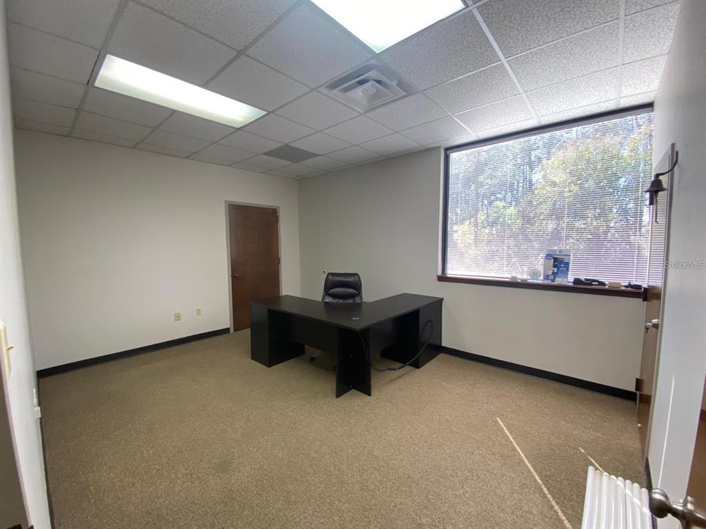 An office room features a black L-shaped desk, beige carpeting, and a large window — 1200 W STATE ROAD 434 UNIT 218, LONGWOOD, FL