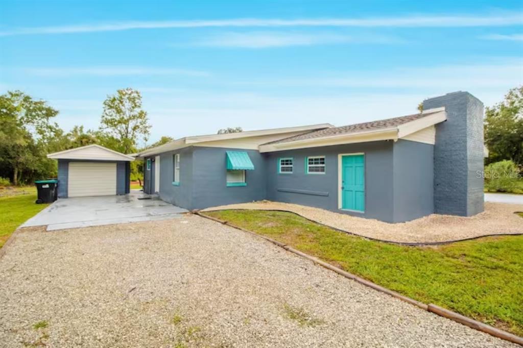A gray single-story house with a teal door, detached garage, and gravel driveway — 1731 GRAYSON DRIVE, ORLANDO, FL