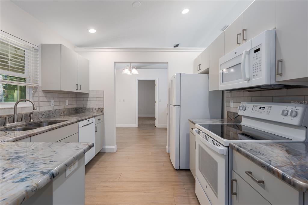A kitchen features light gray cabinets, granite countertops, white appliances, and wood-look tile flooring — 9206 31ST STREET COURT E, PARRISH, FL