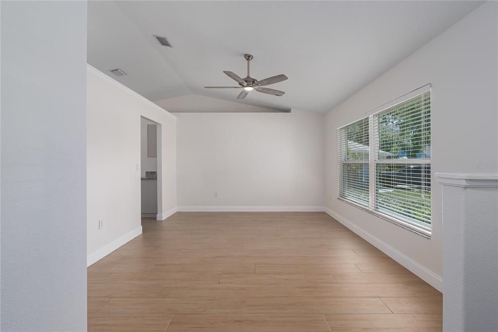 A bright, empty room features light wood-look tile flooring, a ceiling fan, and large windows — 9206 31ST STREET COURT E, PARRISH, FL