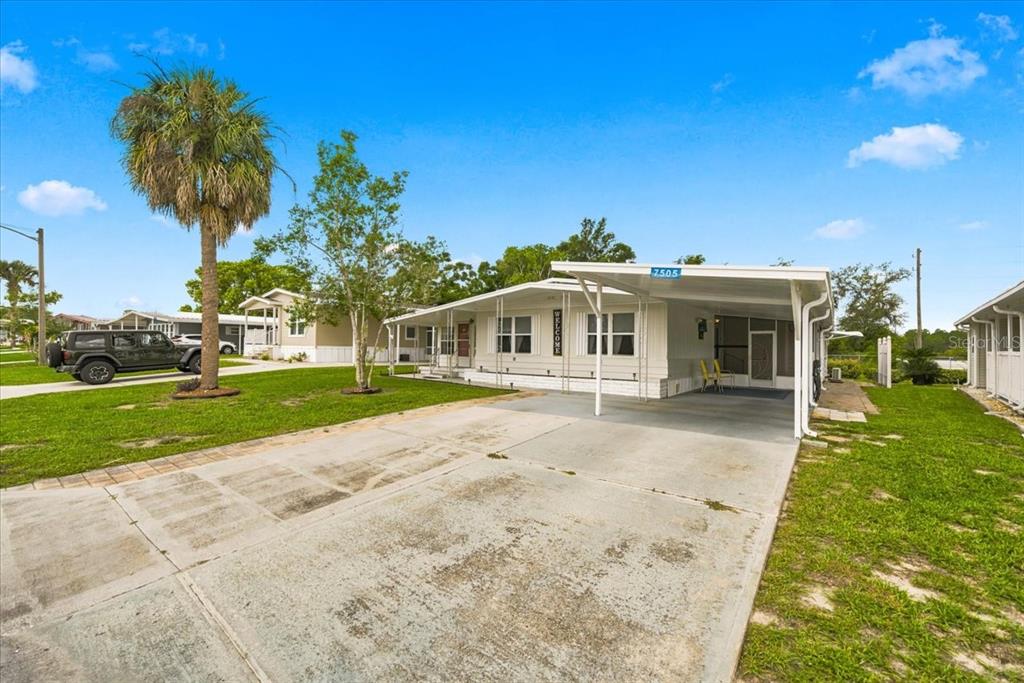 A single-story manufactured home with a carport and a palm tree in the front yard — 7505 FAIRLANE AVENUE, BROOKSVILLE, FL