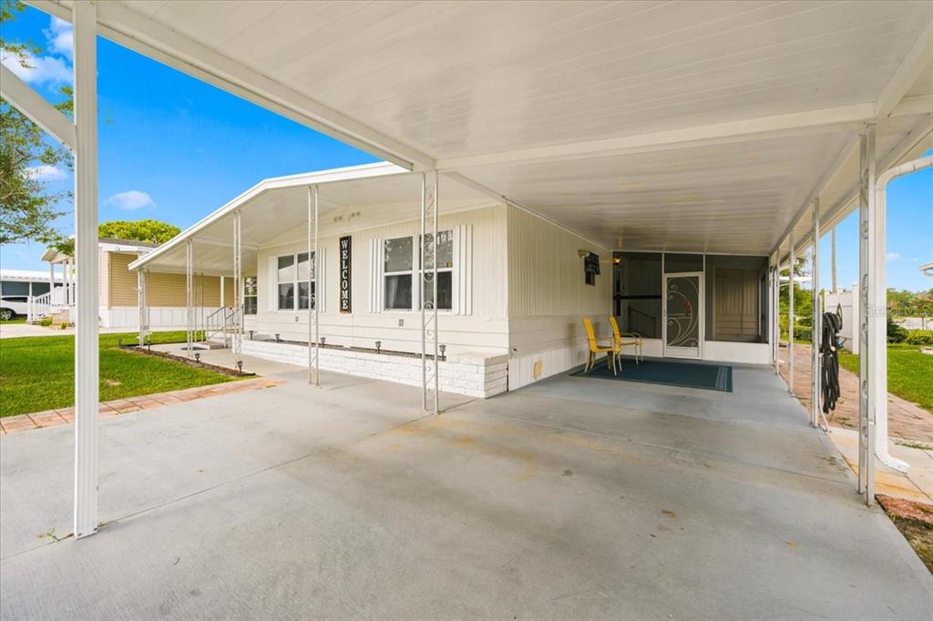 A manufactured home exterior features a large concrete carport, a screened porch, and white siding — 7505 FAIRLANE AVENUE, BROOKSVILLE, FL