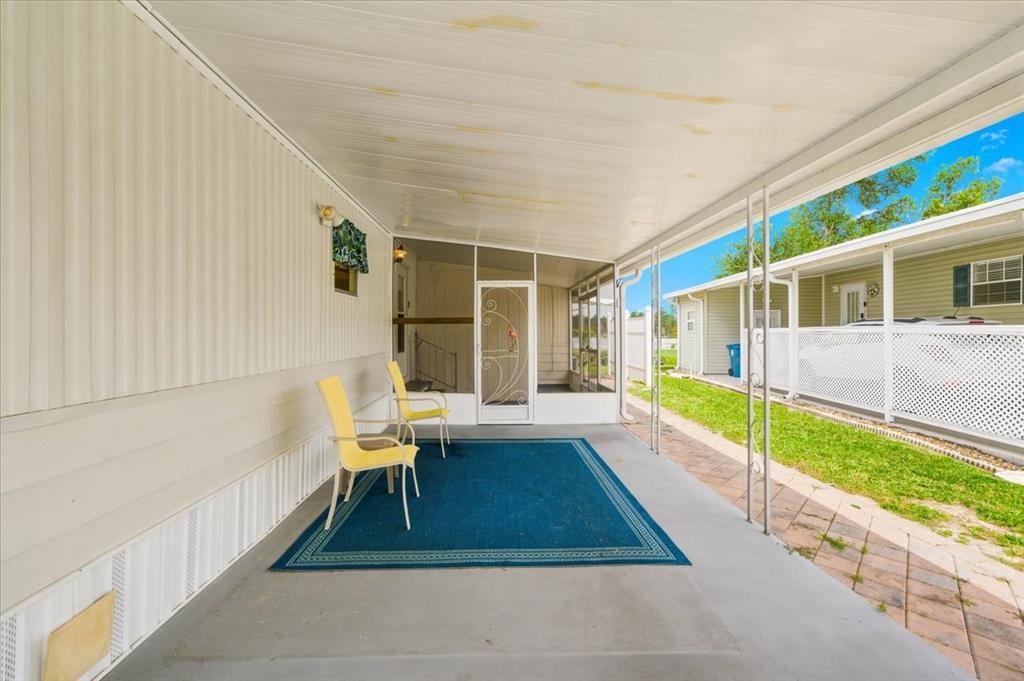 A covered concrete patio features a blue area rug, two yellow chairs, and screen enclosure — 7505 FAIRLANE AVENUE, BROOKSVILLE, FL