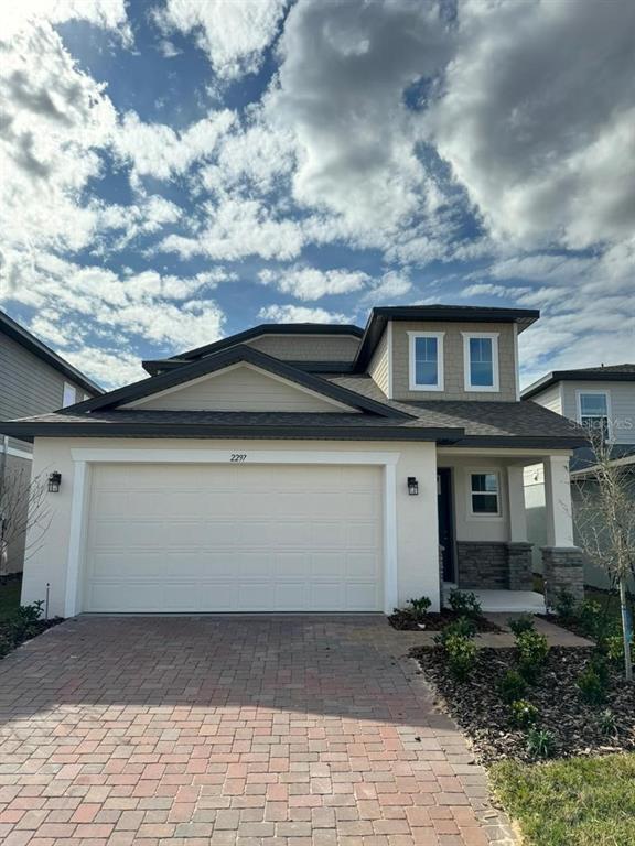 A two-story house with a beige stucco exterior, a brick driveway, and a two-car garage — 2297 TREASURE HILL STREET, MINNEOLA, FL
