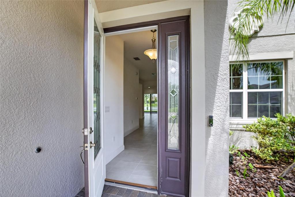 An open front door reveals a tiled entryway with a hanging light fixture — 31142 LINDENTREE DRIVE, WESLEY CHAPEL, FL