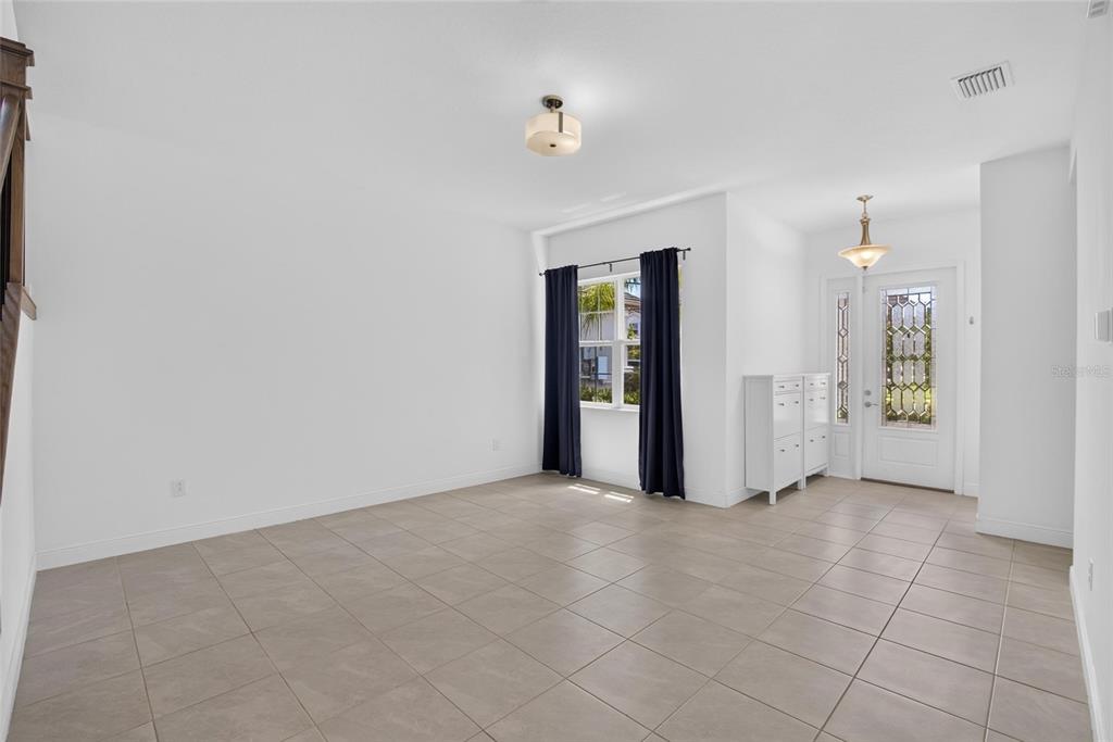 An empty room with light tile flooring, white walls, a window with curtains, and an entryway — 31142 LINDENTREE DRIVE, WESLEY CHAPEL, FL