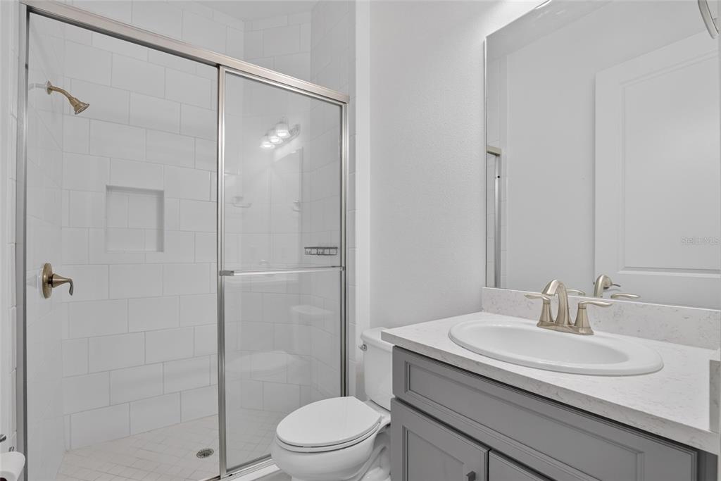 A bathroom features a gray vanity with a white countertop, a toilet, and a glass-enclosed shower — 31142 LINDENTREE DRIVE, WESLEY CHAPEL, FL