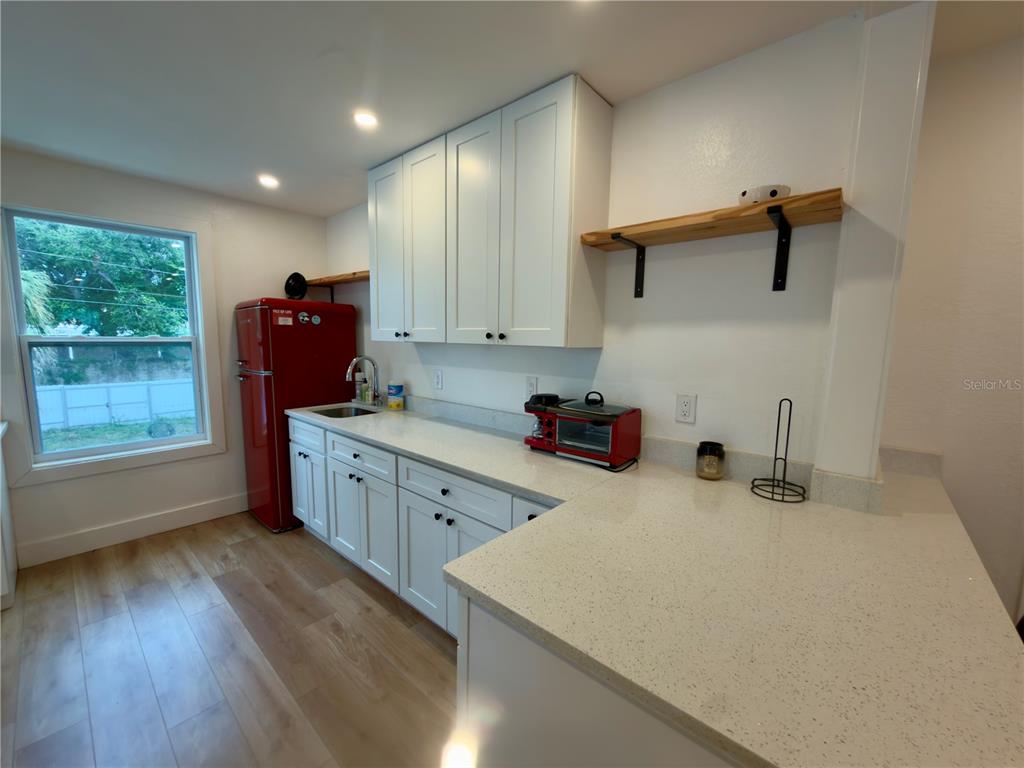 A bright, empty room features light wood-look flooring, white walls, and large windows with curtains — 2238 QUINCY STREET S, ST PETERSBURG, FL