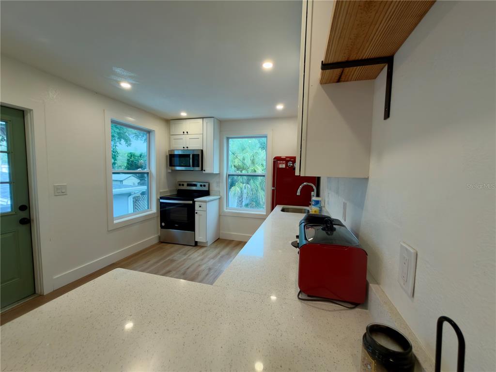 A bright, empty room features light wood-look flooring, white walls, and multiple windows with curtains — 2238 QUINCY STREET S, ST PETERSBURG, FL