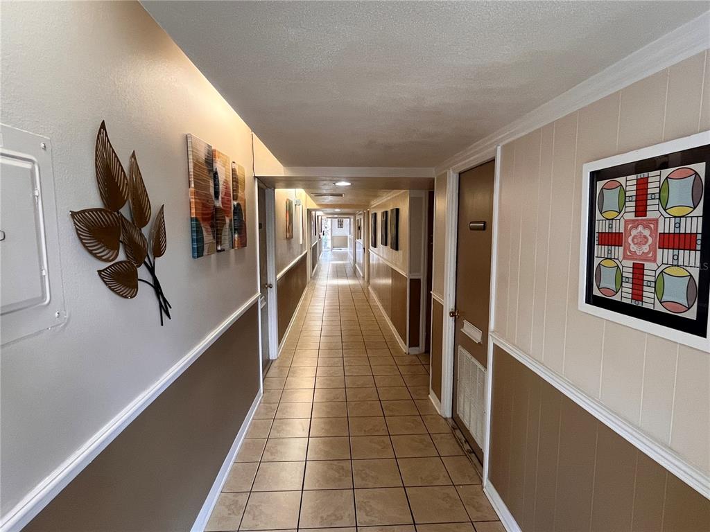 A long, tiled indoor hallway features beige walls with wainscoting and decorative wall art — 141 W CENTRAL AVENUE UNIT 16, WINTER HAVEN, FL