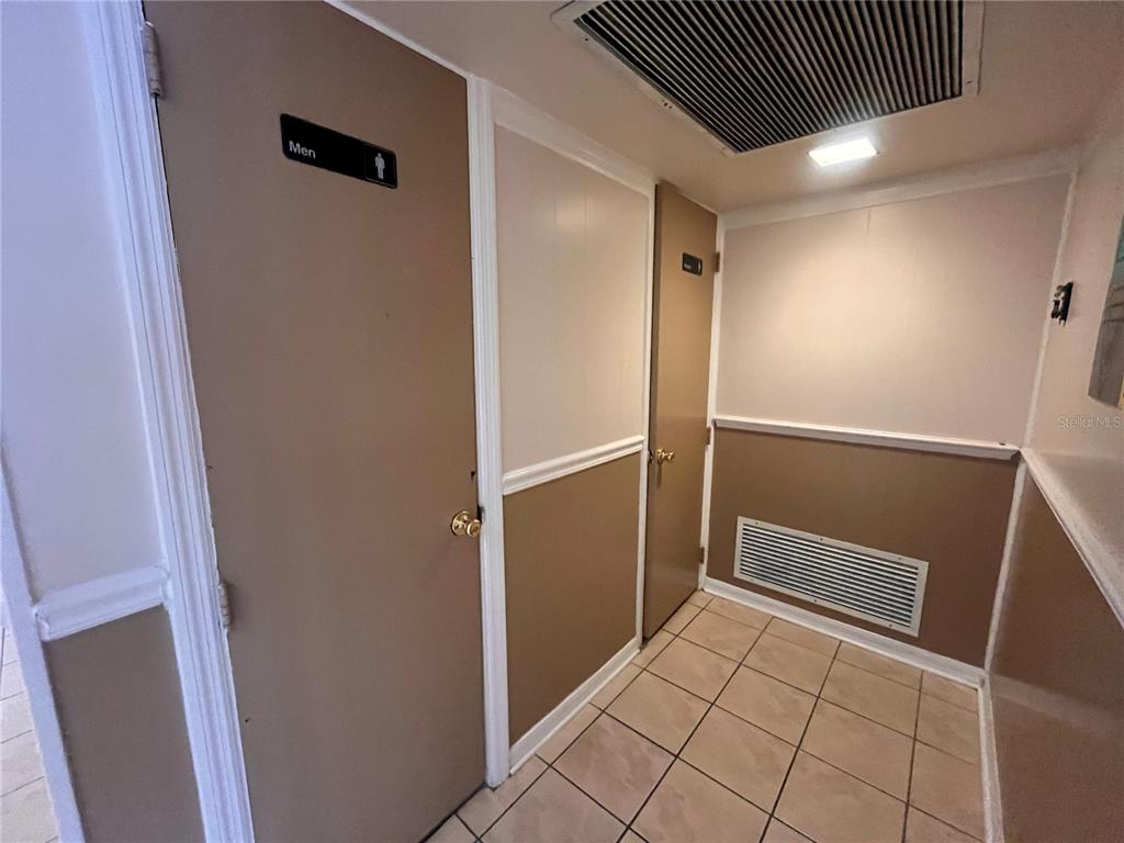 A hallway features beige walls, tiled flooring, a men's restroom door, and a utility closet — 141 W CENTRAL AVENUE UNIT 16, WINTER HAVEN, FL