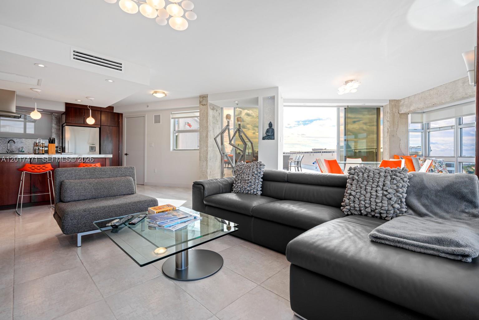 A modern living room features a dark leather sectional, glass coffee table, and open kitchen — MIAMI BEACH, FL