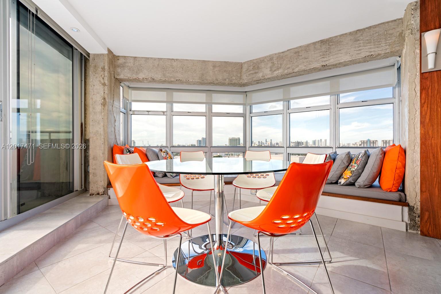A dining area features a glass table, orange chairs, and a window-side built-in bench — MIAMI BEACH, FL