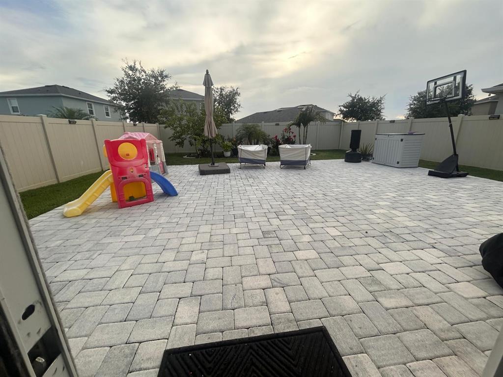 A backyard patio features light gray pavers, a children's play set, and a basketball hoop — 32804 BROOKS HAWK LN, WESLEY CHAPEL, FL