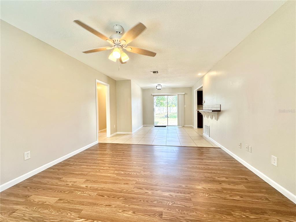 A living room with wood-look flooring transitions to a tiled dining area with sliding doors — 132 S BULOVA DRIVE, APOPKA, FL