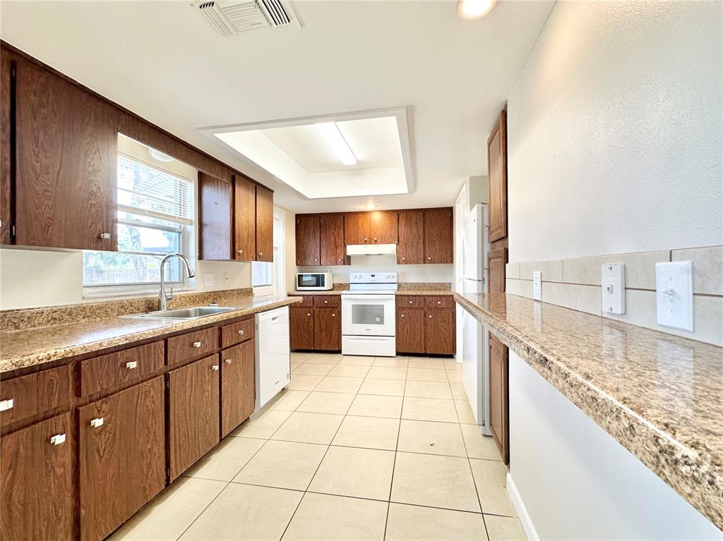 A kitchen features dark wood cabinets, granite countertops, white appliances, and light-colored floor tiles — 132 S BULOVA DRIVE, APOPKA, FL