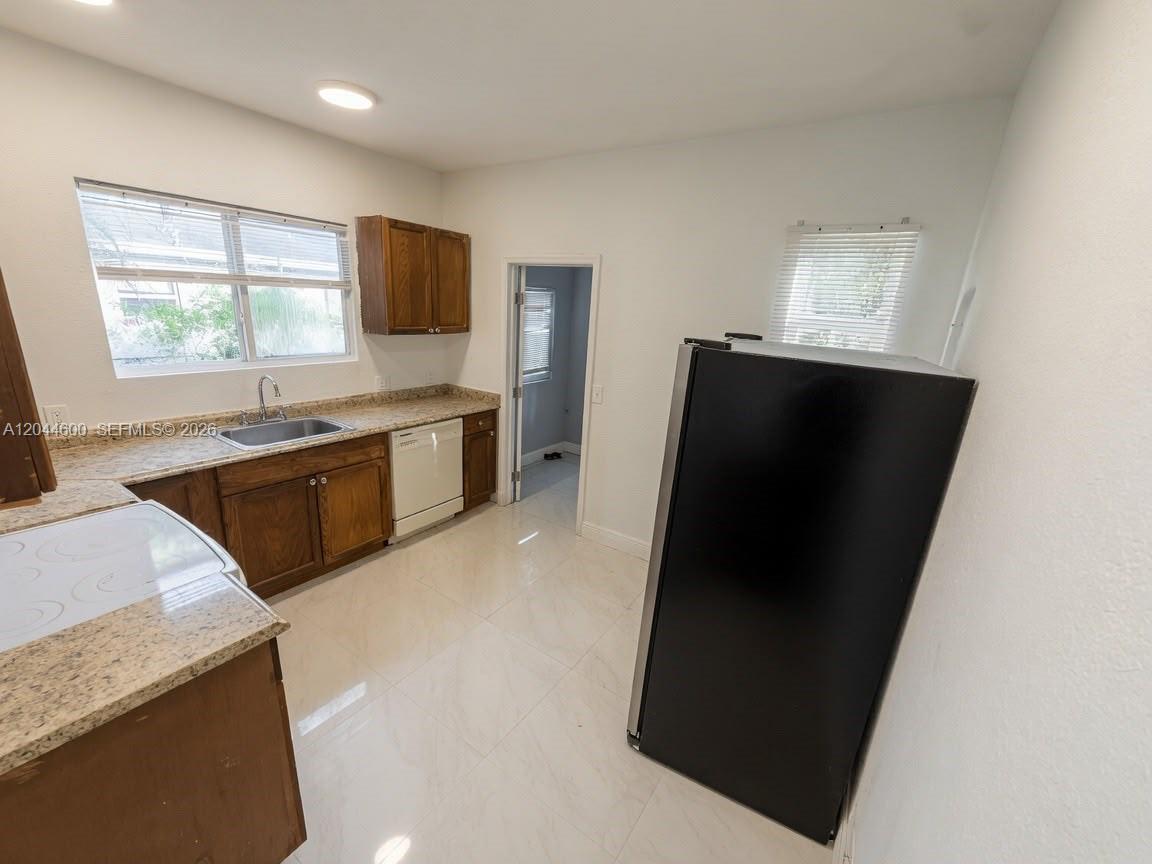 A kitchen features wood cabinets, granite countertops, a black refrigerator, and white tile flooring — 1154 W 25th St # 0, Riviera Beach FL 33404, RIVIERA BEACH, FL