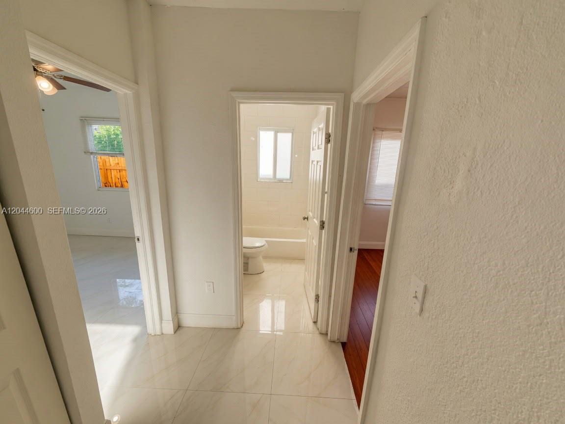 A hallway with white tile flooring leads to a bathroom and two adjacent rooms — 1154 W 25th St # 0, Riviera Beach FL 33404, RIVIERA BEACH, FL