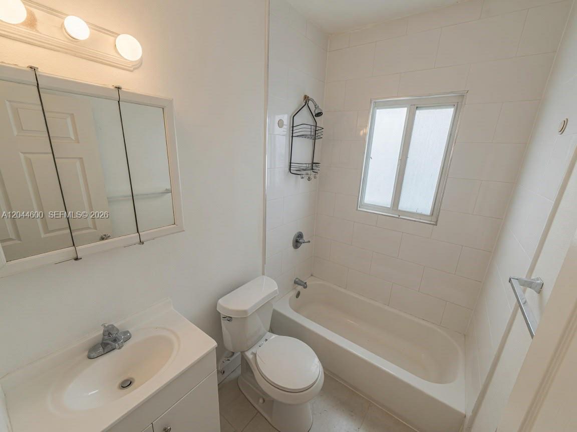 A bathroom features a white vanity, a toilet, and a bathtub with white wall tiles — 1154 W 25th St # 0, Riviera Beach FL 33404, RIVIERA BEACH, FL