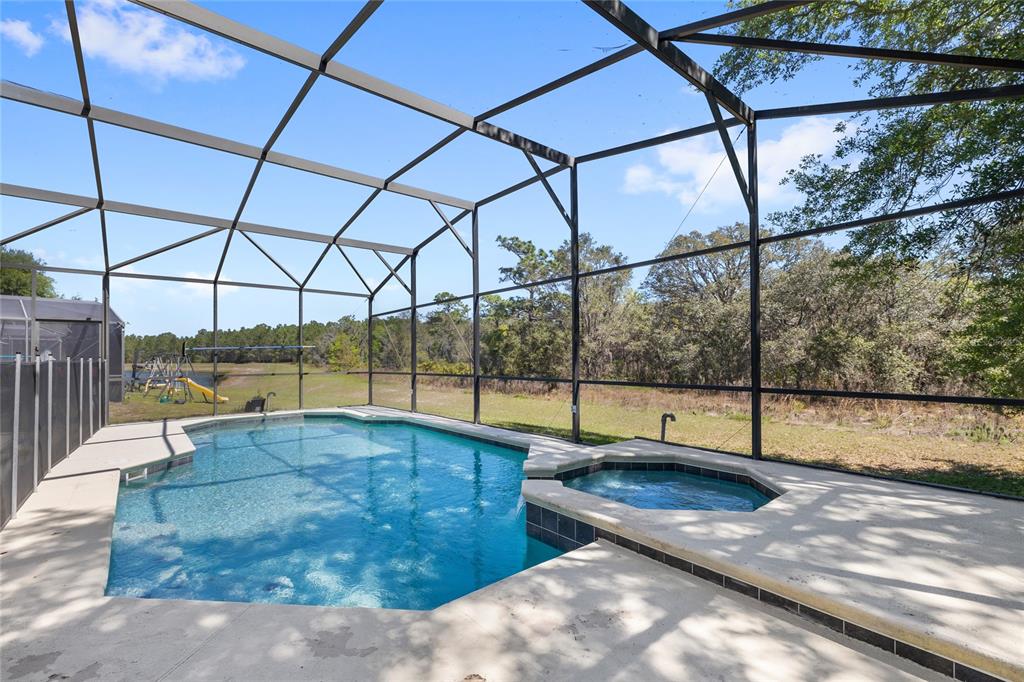 A screened-in swimming pool and attached hot tub sit on a concrete patio overlooking woods — 16943 SUNRISE VISTA DRIVE, CLERMONT, FL