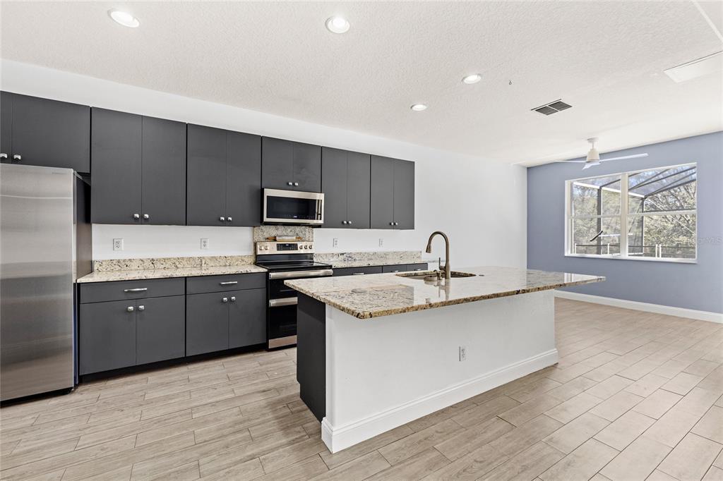 A kitchen features dark gray cabinets, granite countertops, a center island, and light wood flooring — 16943 SUNRISE VISTA DRIVE, CLERMONT, FL