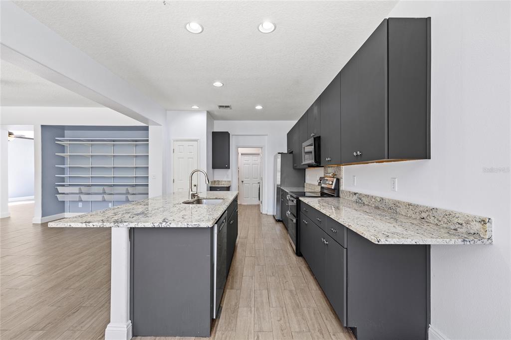 A kitchen features dark gray cabinets, granite countertops, and light wood-look tile flooring — 16943 SUNRISE VISTA DRIVE, CLERMONT, FL