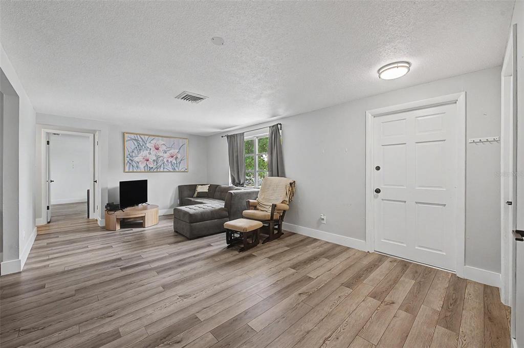 A living room features light gray walls, wood-look flooring, a sectional sofa, and a front door — 11592 110TH TERRACE, LARGO, FL