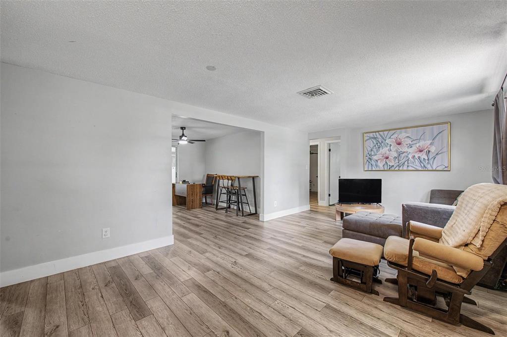 A living room with light wood-look flooring, gray walls, and an adjacent dining area — 11592 110TH TERRACE, LARGO, FL