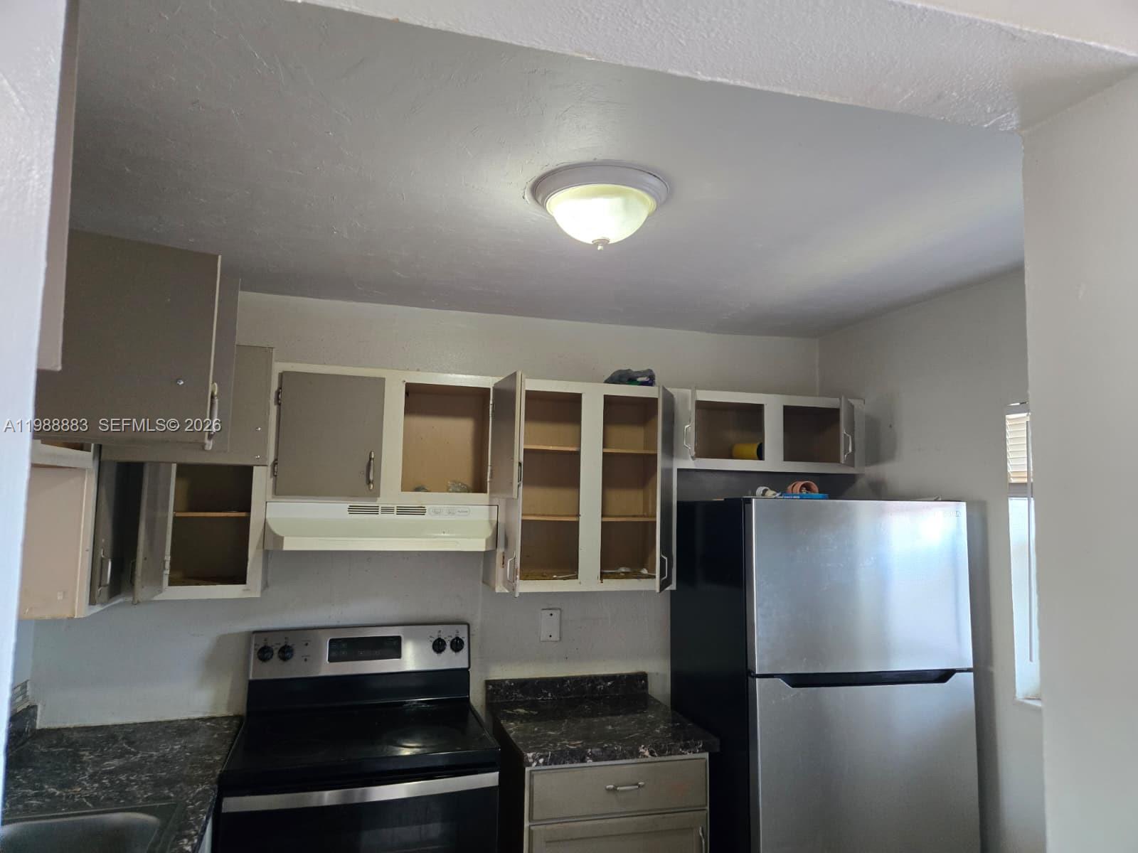 A kitchen features dark countertops, stainless steel appliances, and upper cabinets with some missing doors — 19791 SW 114th Ave # 335, Miami FL 33157, MIAMI, FL