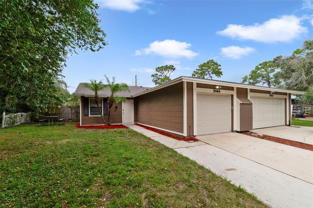 A brown single-story duplex with two garage doors and a front lawn under a blue sky — 5444 PEACO PLACE, WINTER PARK, FL