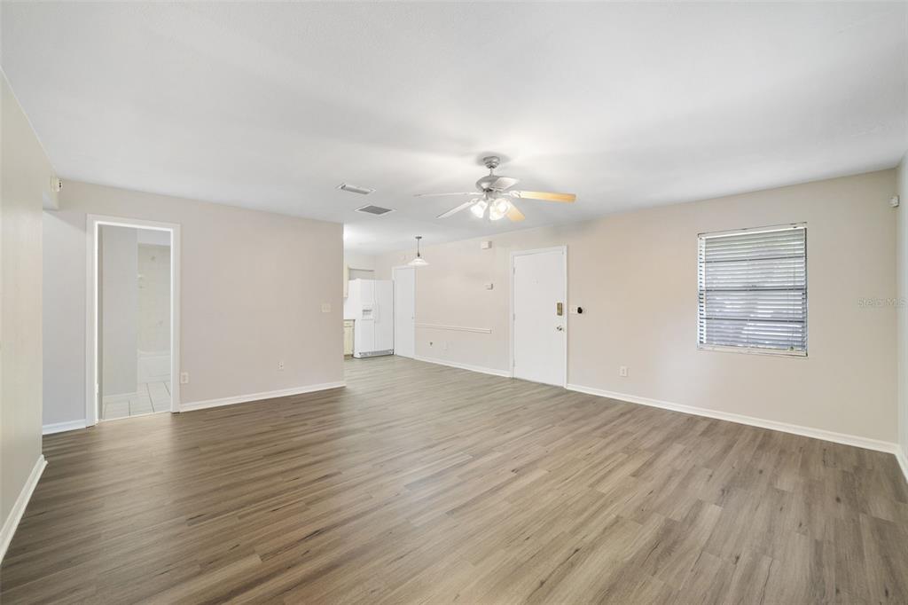 An empty living room with light wood-look flooring, a ceiling fan, and a white door — 5444 PEACO PLACE, WINTER PARK, FL