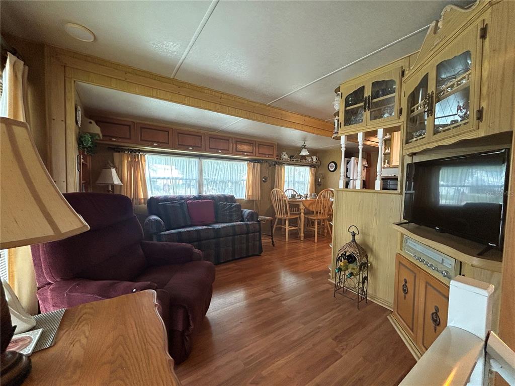 A living room with wood flooring, a maroon recliner, a patterned sofa, and wooden cabinetry — 2 WOODRUFF WAY, LAKE WALES, FL