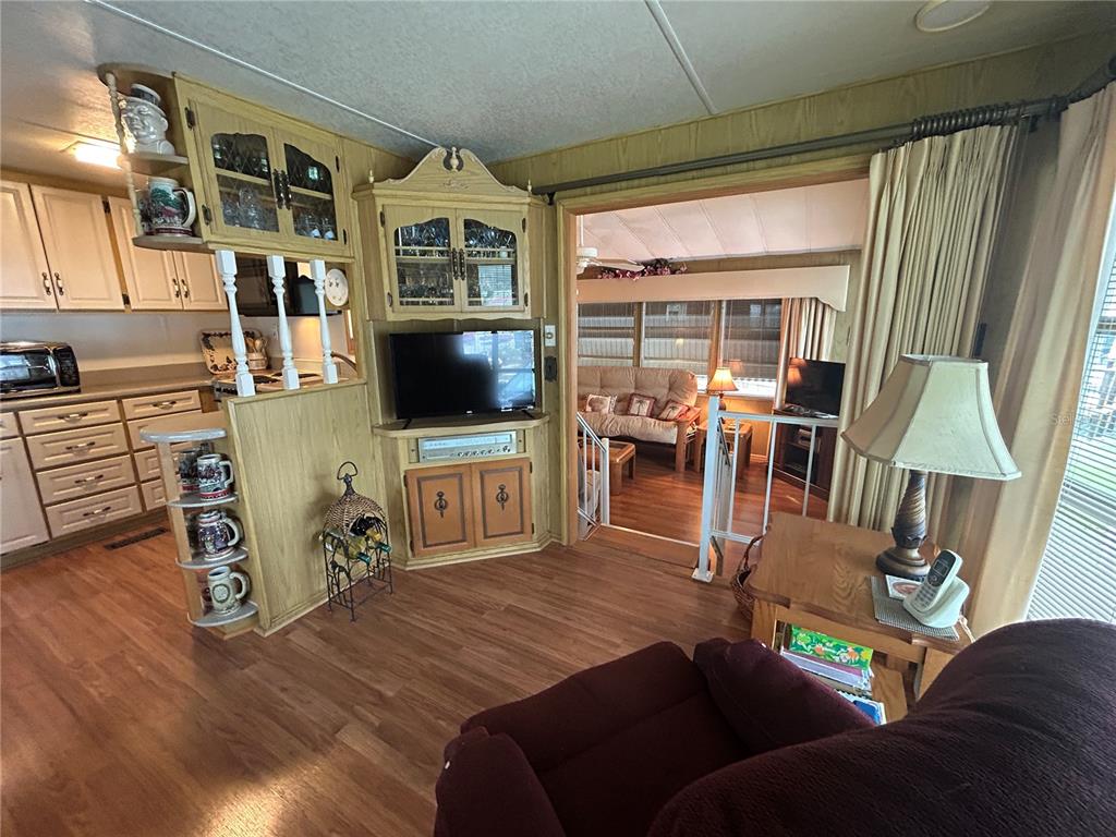 A living room with wood-look flooring, a built-in media cabinet, and a view into a sunroom — 2 WOODRUFF WAY, LAKE WALES, FL