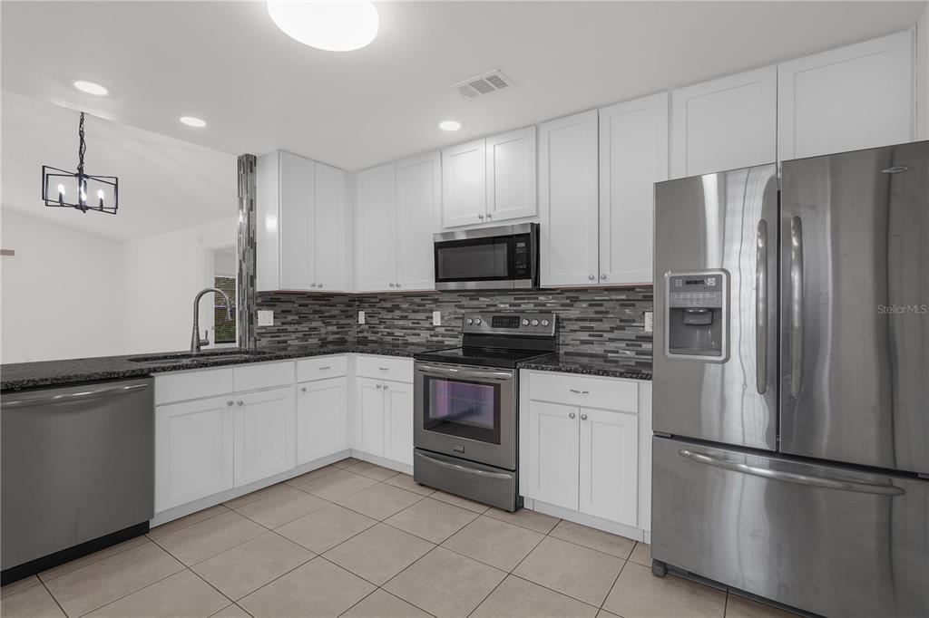 A kitchen features white cabinets, stainless steel appliances, a dark tile backsplash, and tiled floors — 1455 ELDRA DRIVE, KISSIMMEE, FL