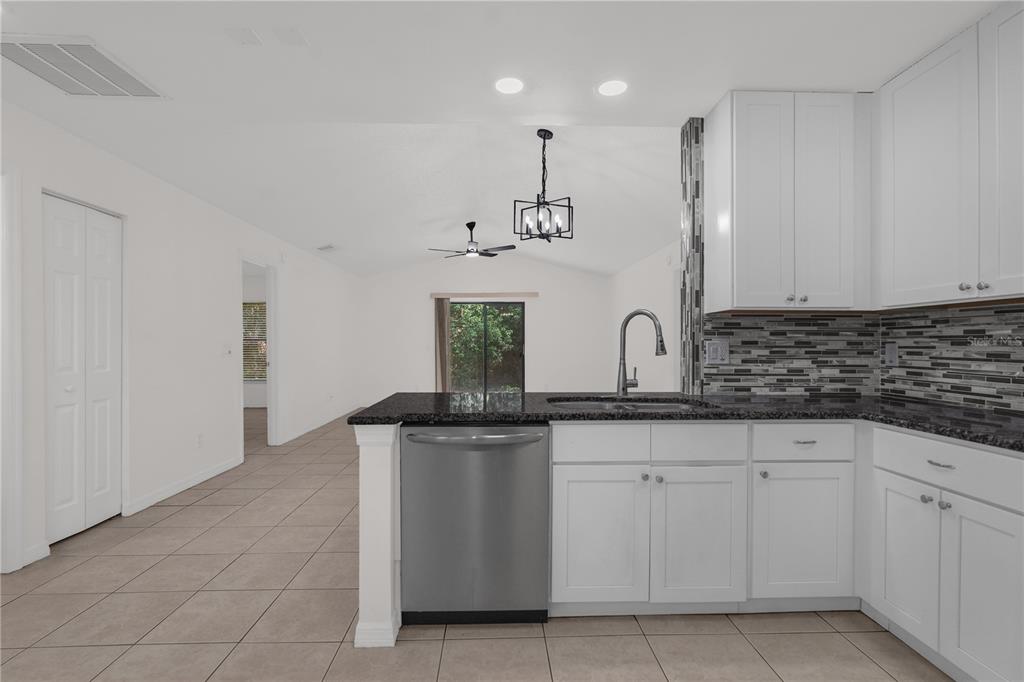 A kitchen with white cabinets, granite countertops, and a stainless steel dishwasher overlooks a living area — 1455 ELDRA DRIVE, KISSIMMEE, FL