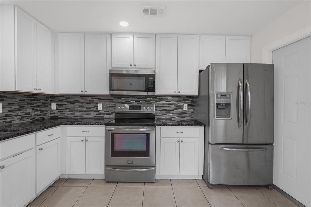 A kitchen with white cabinets, stainless steel appliances, and a dark tiled backsplash — 1455 ELDRA DRIVE, KISSIMMEE, FL