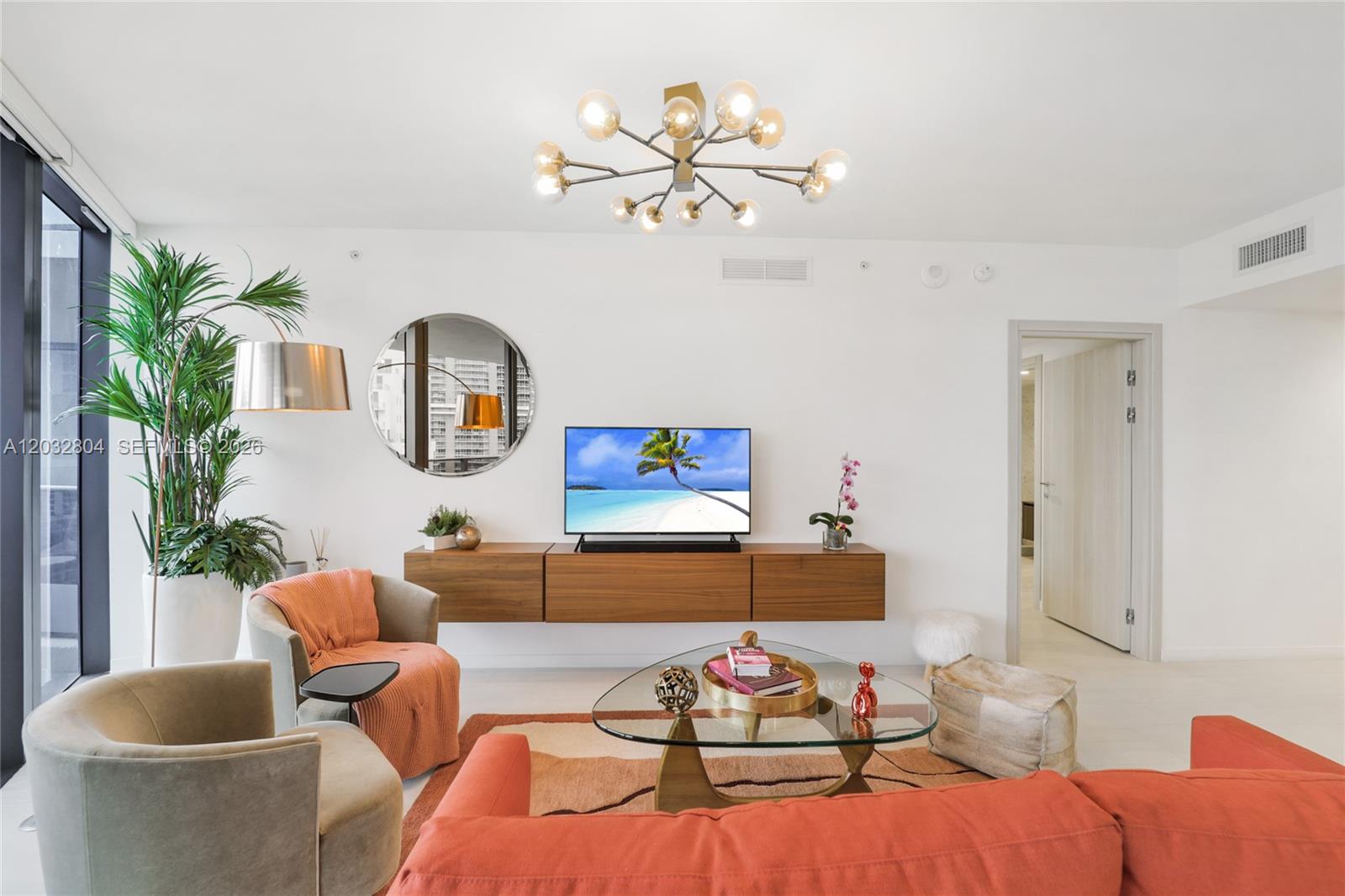 A modern living room features a floating wooden console, orange sofa, and a glass chandelier — 1000 Brickell Plz # 4401, Miami FL 33131, MIAMI, FL