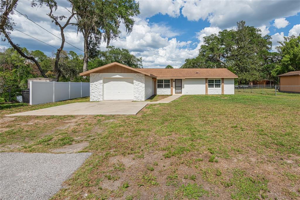 A single-story house with a white stone-accented garage and a brown shingled roof — 19823 ALABAMA ROAD, SPRING HILL, FL
