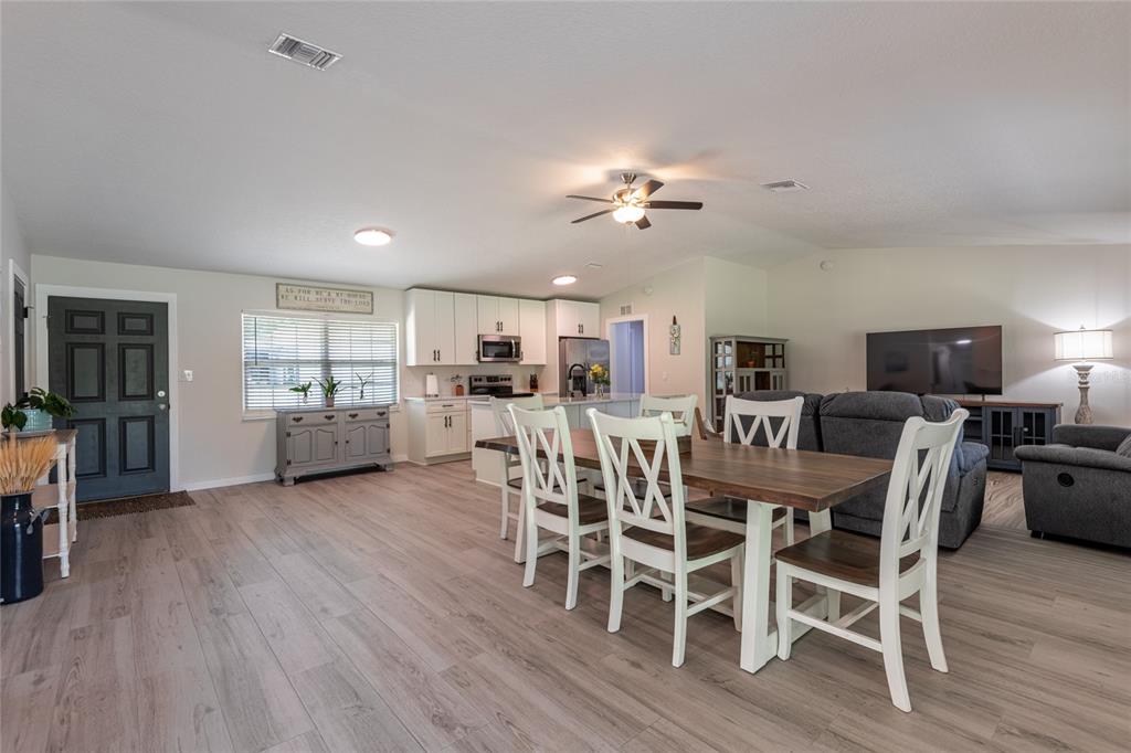 An open-concept living and dining area features light wood flooring, white cabinets, and a ceiling fan — 19823 ALABAMA ROAD, SPRING HILL, FL