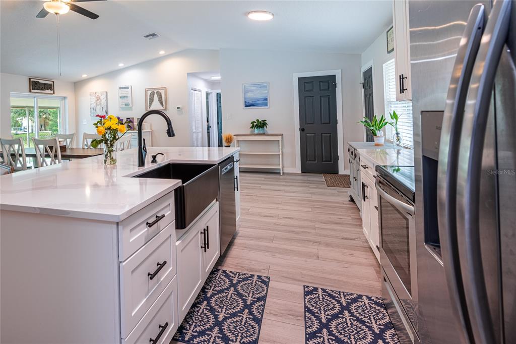 A modern kitchen features white cabinetry, a farmhouse sink, and light wood-look flooring — 19823 ALABAMA ROAD, SPRING HILL, FL