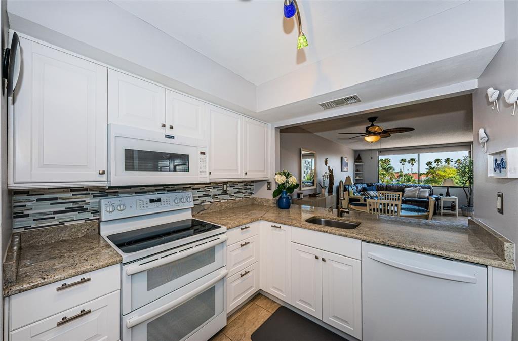 A kitchen with white cabinets, granite countertops, stainless steel appliances, and a view into the living room — 6295 BAHIA DEL MAR CIRCLE UNIT 405, ST PETERSBURG, FL