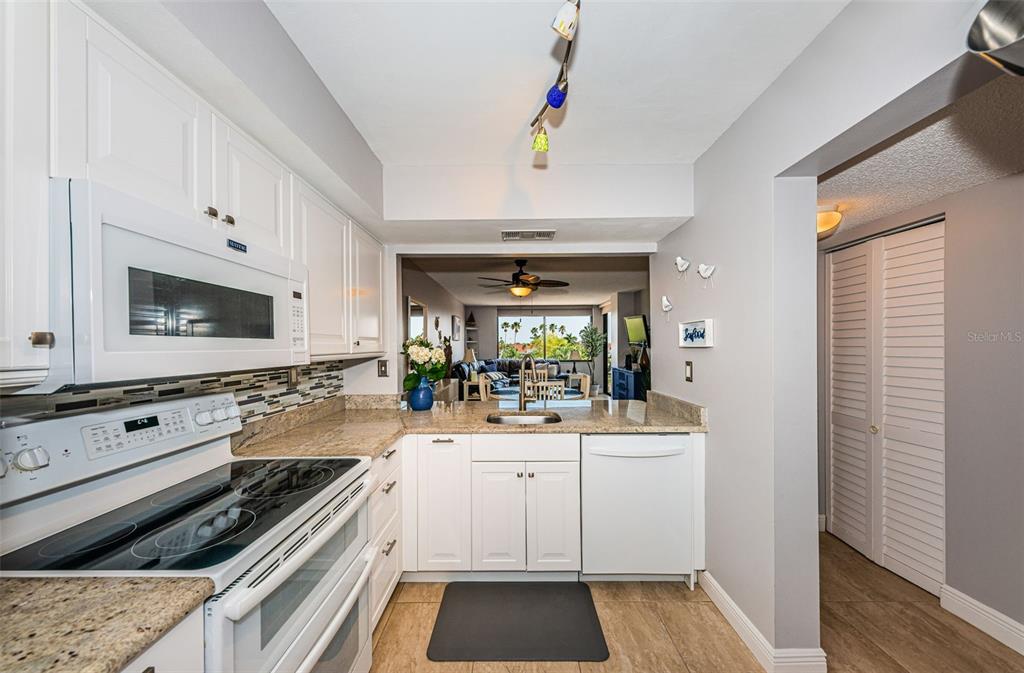 A kitchen with white cabinets, granite countertops, and stainless steel appliances overlooks a living area — 6295 BAHIA DEL MAR CIRCLE UNIT 405, ST PETERSBURG, FL