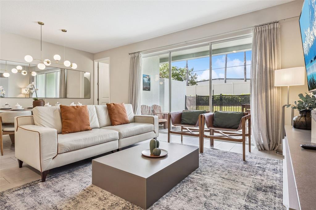 A living room with a white sofa, coffee table, two armchairs, and sliding glass doors — 7952 FORMOSA VALLEY PLACE, KISSIMMEE, FL