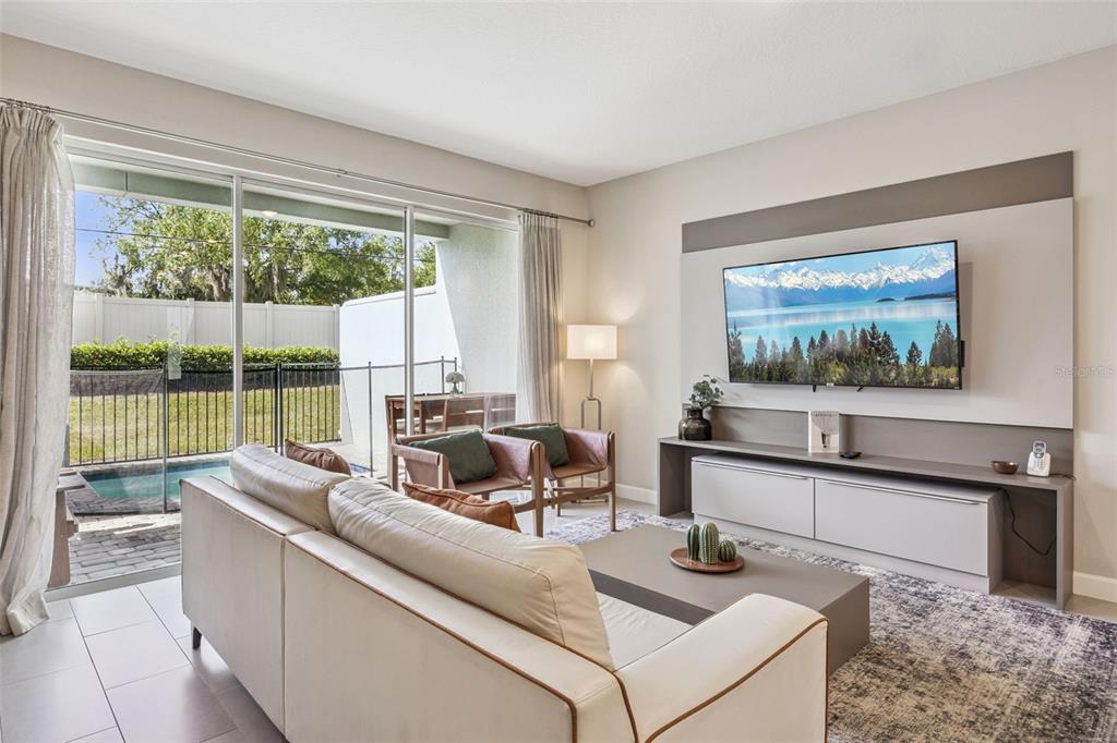 A living room features a sofa, television, media console, and sliding doors opening to a pool — 7952 FORMOSA VALLEY PLACE, KISSIMMEE, FL