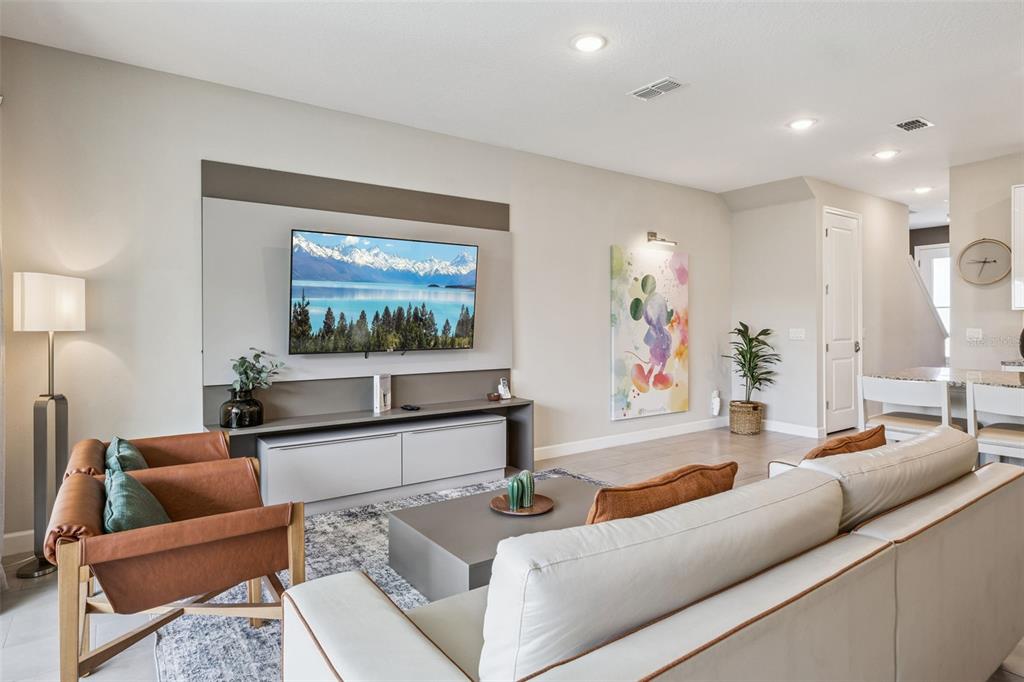 A living room features a wall-mounted television, a grey media console, and modern furniture — 7952 FORMOSA VALLEY PLACE, KISSIMMEE, FL