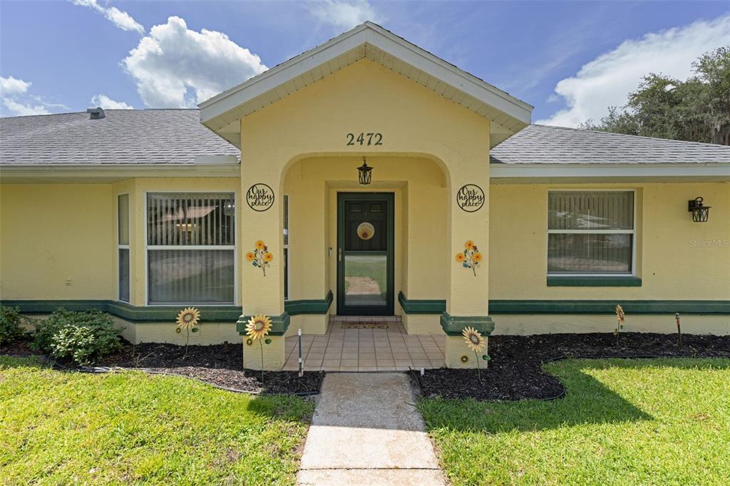 The exterior of a yellow house features a covered entryway, a walkway, and sunflower decorations — 2472 CR 447, LAKE PANASOFFKEE, FL