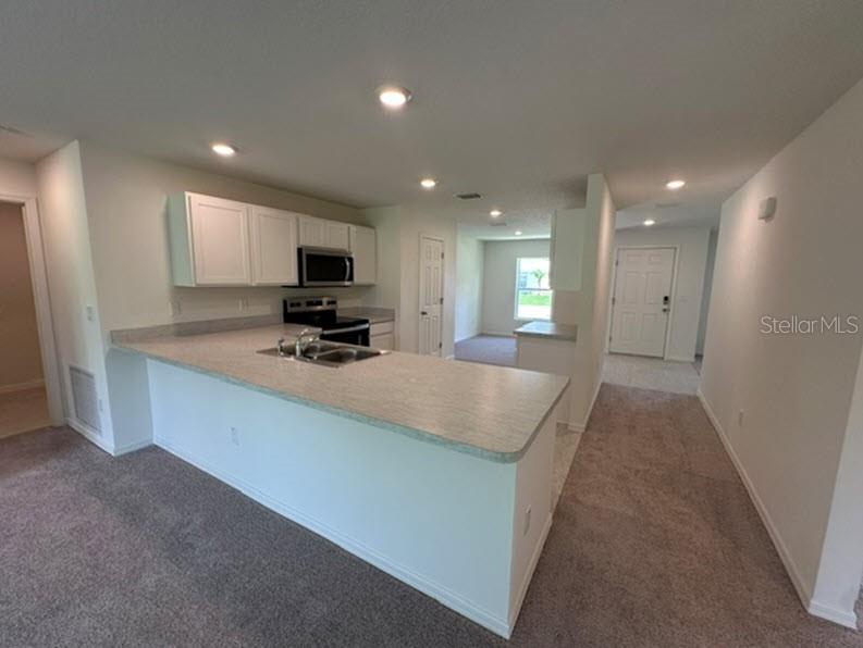 A kitchen with white cabinets and a breakfast bar overlooks a carpeted living area — 91 RANDOLPH DRIVE, PALM COAST, FL