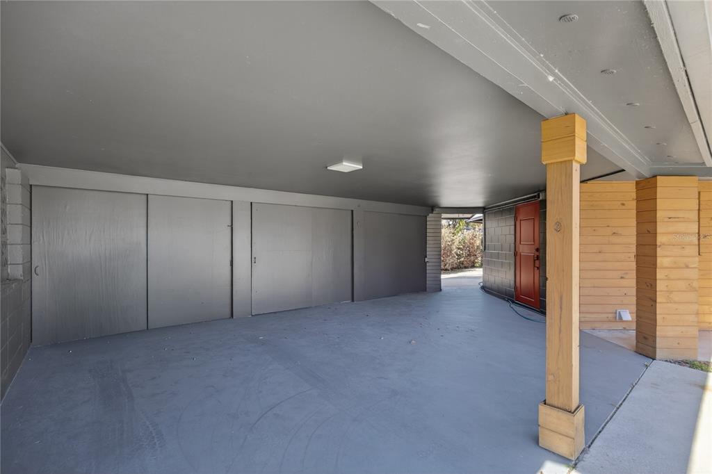 A covered carport features a gray concrete floor, wood-paneled support columns, and a red door — 1503 CANAL COURT, TAVARES, FL