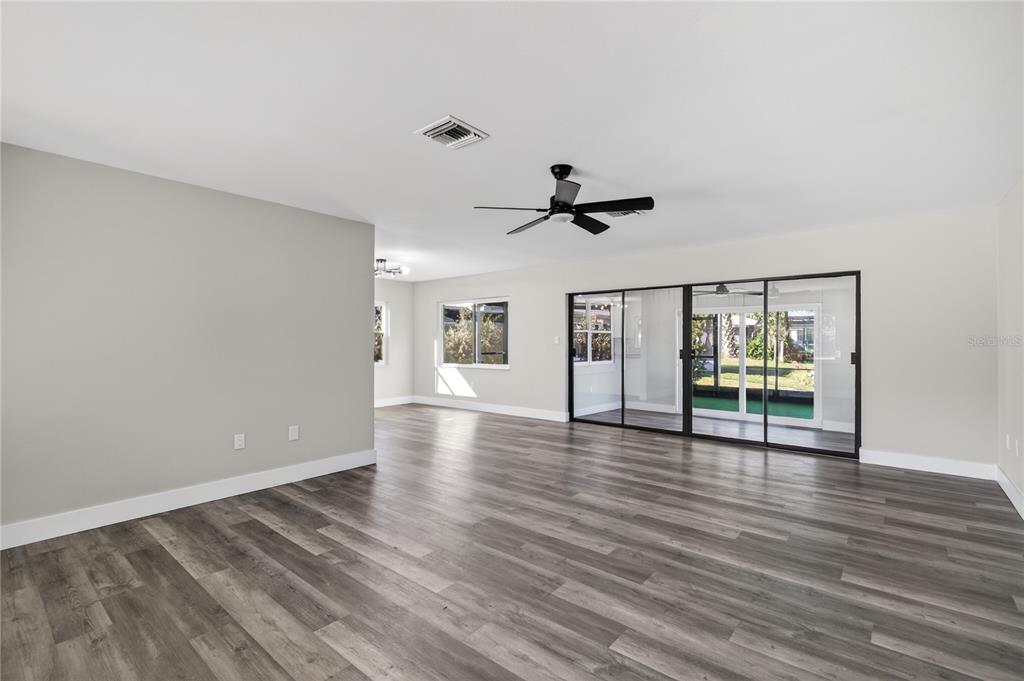 A spacious living room features gray wood-look flooring, a ceiling fan, and large sliding glass doors — 1503 CANAL COURT, TAVARES, FL